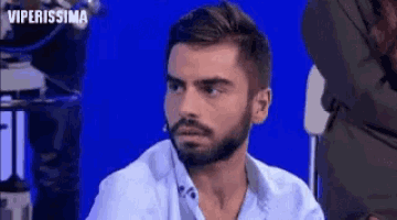 a man with a beard is sitting in front of a blue background and looking at the camera .
