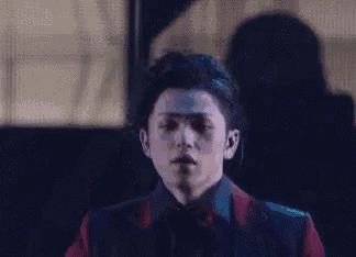 a young man in a red suit and black tie is standing in front of a piano .