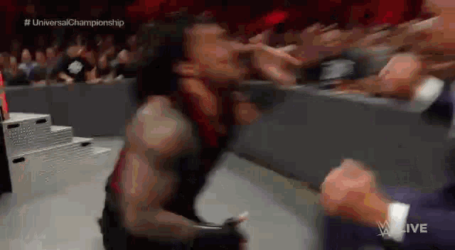 roman reigns is fighting a wrestler in a wrestling match while a crowd watches .