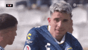 a man in a blue jersey with the letter c on it is talking to another man .