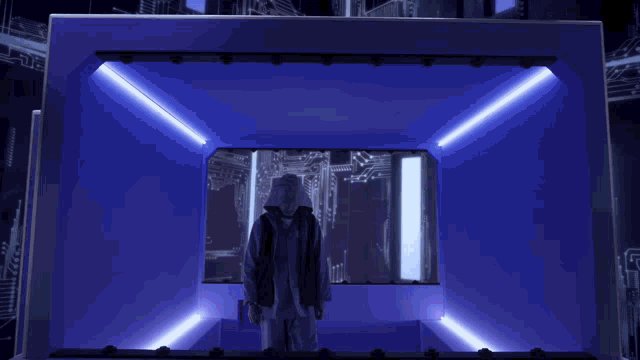a man in a hooded jacket is standing in a room with blue lights behind him