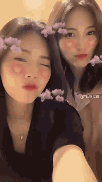 two young women are taking a selfie together with purple flowers on their faces .