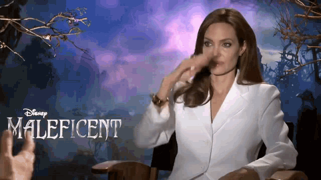 a woman in a white suit is sitting in front of a disney maleficent poster