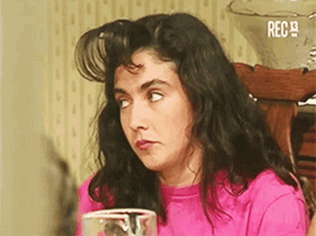 a woman in a pink shirt is sitting at a table with a glass in front of her and the words rec 9 on the bottom