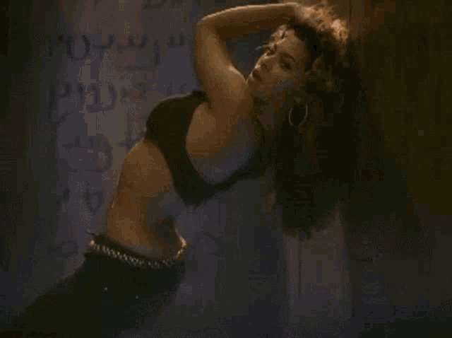 a woman in a black bra is dancing in front of a wall that has arabic writing on it