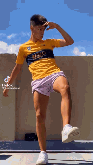 a young man in a yellow shirt and purple shorts is kicking his leg in the air .