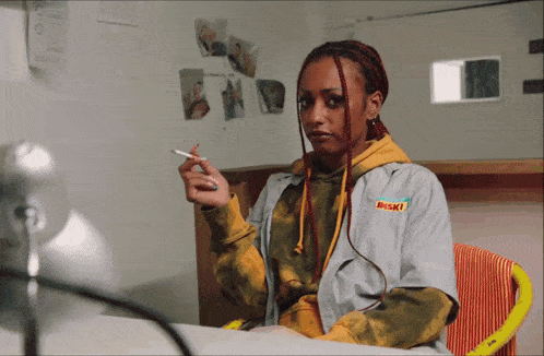 a woman is smoking a cigarette and wearing a jacket that says ' waski ' on it