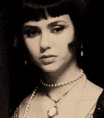 a black and white photo of a woman wearing a choker and pearls .
