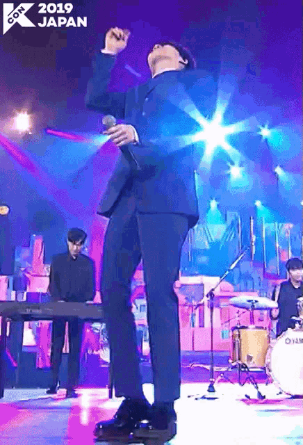 a man in a suit is singing into a microphone on a stage with the year 2019 japan on the bottom