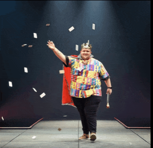 a man wearing a crown and a cape is walking on stage