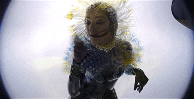 a woman is wearing a mask and a necklace with flowers on her neck .