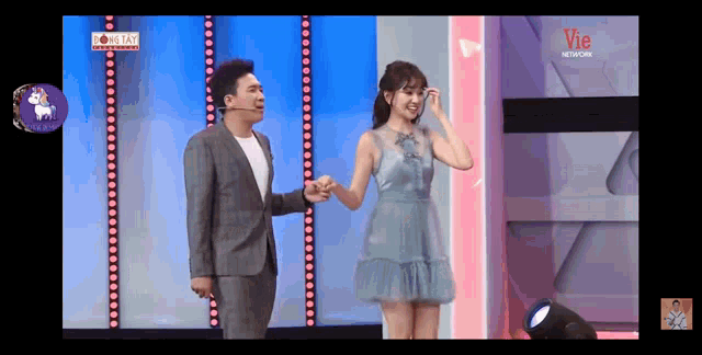 a man and a woman holding hands on a stage in front of a sign that says vie