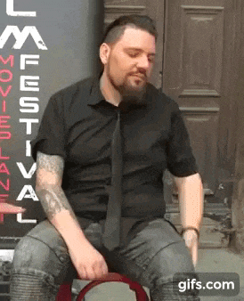 a man in a black shirt and tie is sitting in front of a sign that says movie festival .
