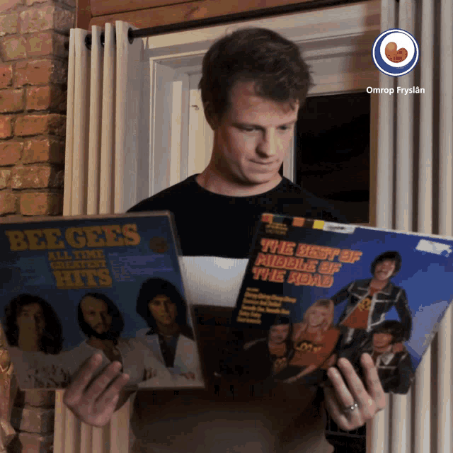 a man is holding two records in his hands one of which says beegees