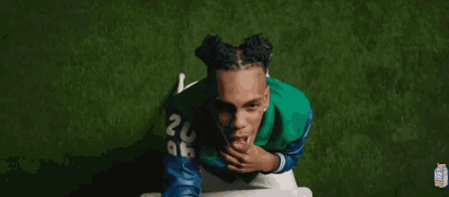 a man wearing a green and blue varsity jacket is covering his face with his hand .