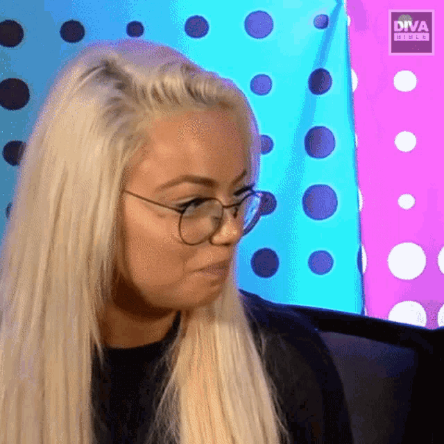 a woman wearing glasses and a black shirt is sitting in front of a colorful wall with polka dots .