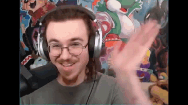 a man wearing headphones and glasses is smiling and waving in front of a microphone .