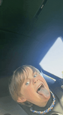 a young boy sticking his tongue out and wearing a necklace