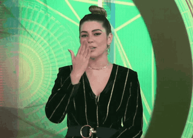 a woman covering her mouth with her hand while wearing a striped jacket