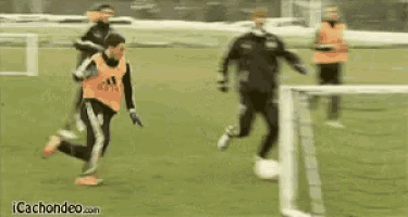 a soccer player wearing an orange adidas vest is kicking a ball