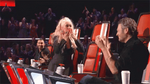 a man and a woman are sitting in a stadium with their arms outstretched and clapping .