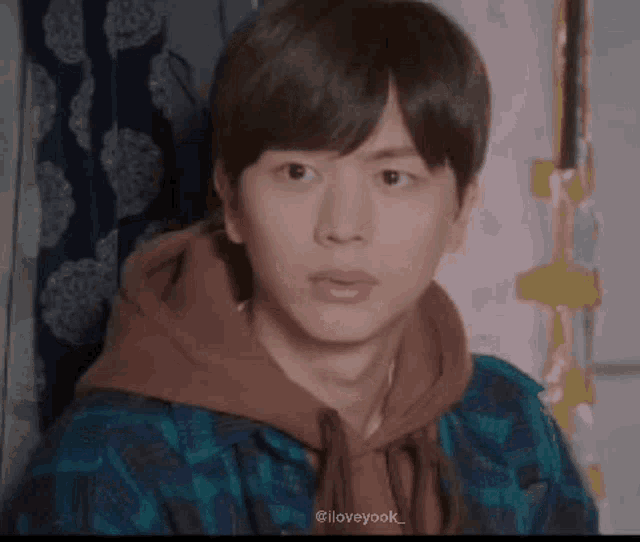 a young man wearing a plaid shirt and a brown hoodie is making a funny face .