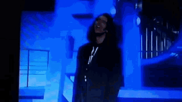 a man with long hair is standing in front of a microphone in a dark room .