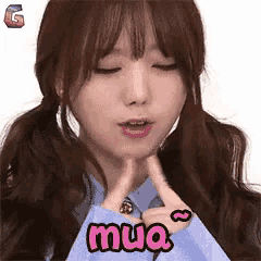 a girl with pigtails is making a heart with her fingers and the word mua is on her shirt
