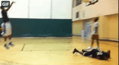 a man is laying on the floor while a basketball player jumps over him .