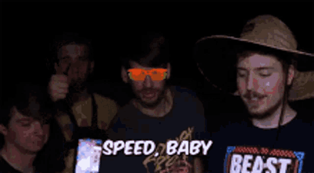 a group of men are standing in a dark room with one wearing a speed baby beast shirt
