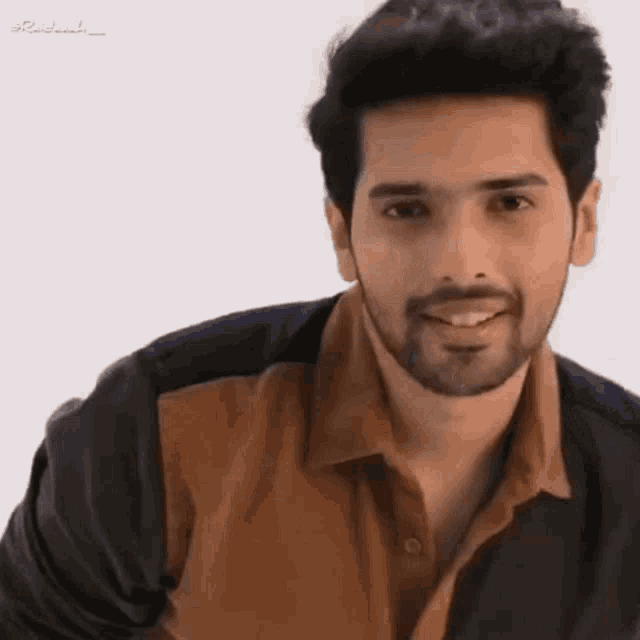 a man with a beard is smiling and wearing a brown shirt .