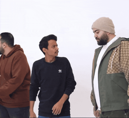 a man wearing a black adidas sweatshirt is standing next to two other men
