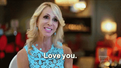a woman in a blue lace dress is sitting in a chair and smiling while saying `` i love you '' .