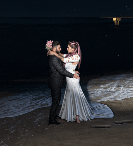 a bride and groom pose for a picture on the beach