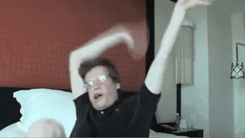 a man wearing glasses is laying on a bed with his arms in the air .