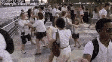 a large group of people are dancing on a sidewalk in a park .