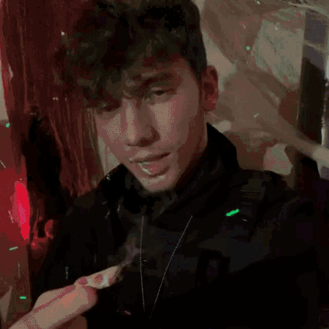 a young man wearing a black turtleneck and a necklace is looking down