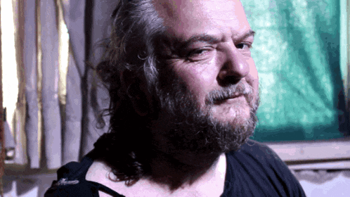 a man with long hair and a beard looks at the camera