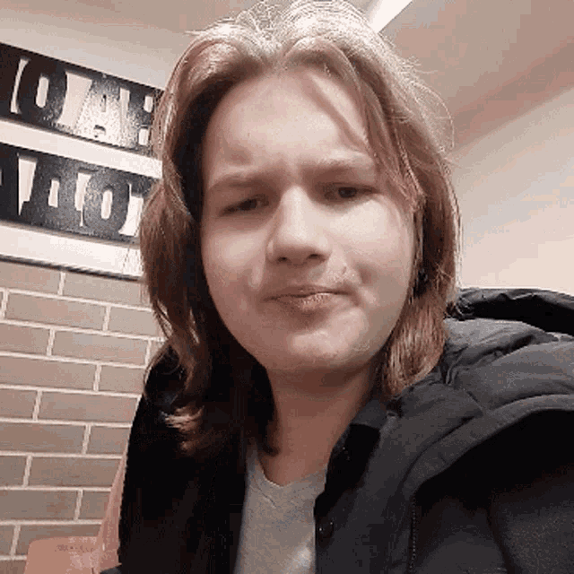 a young man with long hair looks at the camera in front of a sign that says ' oak ' on it