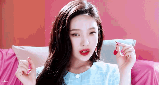 a woman in a blue shirt is holding a small red cherry in her hand