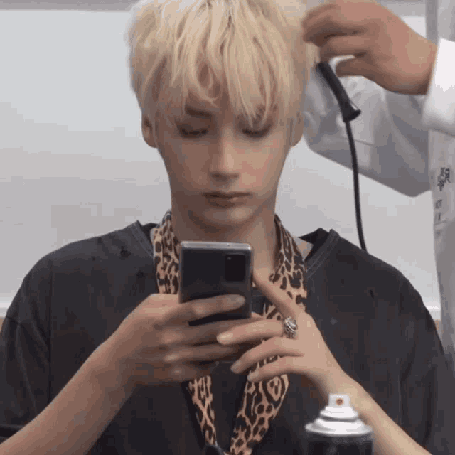 a man with blonde hair is getting his hair styled and looking at his phone