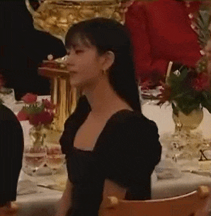 a woman in a black dress is sitting at a table in a restaurant .