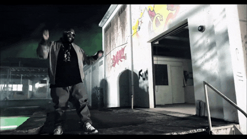 a man is standing in front of a building with graffiti on it that says " fun "