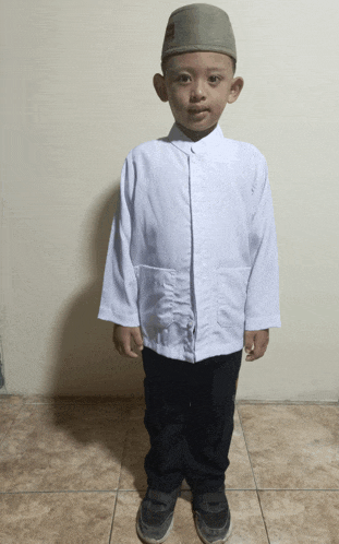 a young boy wearing a white shirt and black pants stands on a tiled floor