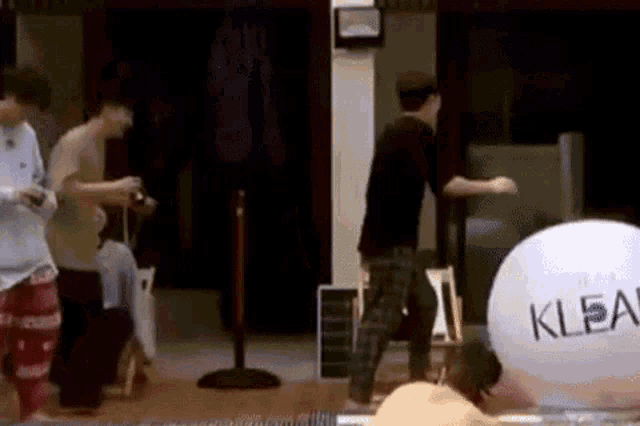 a group of people are standing around a swimming pool with a large white ball that says klean on it .