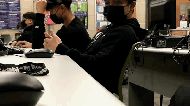 a man wearing a mask sits at a desk with a lanyard that says team bee