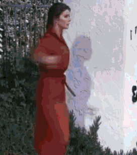 a woman in a red dress is standing in front of a white wall with a clock on it .