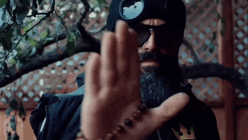 a man with a beard wearing sunglasses and a goggles is making a stop sign