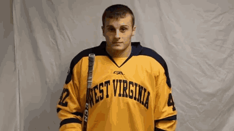 a man wearing a yellow west virginia jersey holds a hockey stick