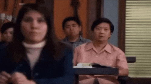 a group of people are sitting in a classroom and one of them is looking at the camera .